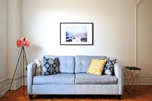 Szara sofa z poduszkami i obrazem na ścianie w jasnym salonie
